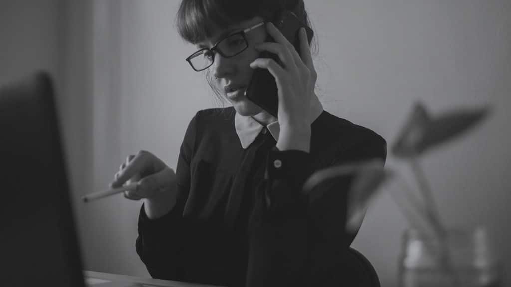 Frau am telefonieren, während sie mit einem Stift auf ihren Laptop-Bildschirm zeigt.